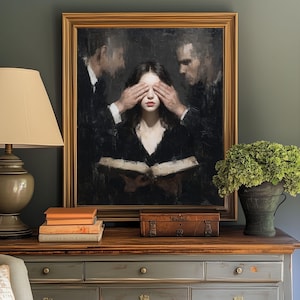 Puede incluir: Pintura al &oacute;leo enmarcada que representa a una mujer con los ojos cubiertos por dos hombres, sosteniendo un libro abierto. Una l&aacute;mpara, libros y una peque&ntilde;a caja est&aacute;n sobre una mesa de madera. Tambi&eacute;n hay un jarr&oacute;n con flores verdes.
