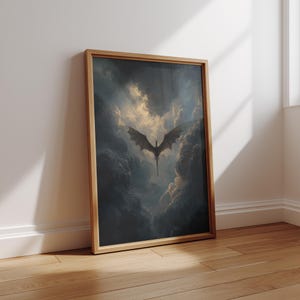 May include: A framed art print depicting a dragon in flight amidst a dramatic, cloudy sky. The dragon's silhouette is set against a bright, golden light, with dark, ominous clouds. The frame is light brown, and the artwork leans against a white wall.