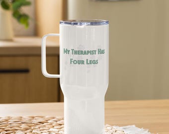Pode incluir: Caneca de viagem branca com uma alça e uma tampa transparente. A caneca tem o texto "My Therapist Has Four Legs" em verde. A caneca está em uma mesa de madeira.