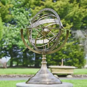 Puede incluir: Una esfera armilar de bronce, un globo celeste, se exhibe al aire libre. La esfera presenta anillos que se cruzan con signos del zodíaco, incluidos Cáncer y Leo. El acabado antiguo y el diseño intrincado crean una estética vintage.