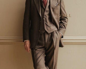 May include: A three-piece brown suit with a white dress shirt and a red tie. The suit includes a jacket, vest, and trousers. The suit is tailored and has a pocket square. The shoes are black.