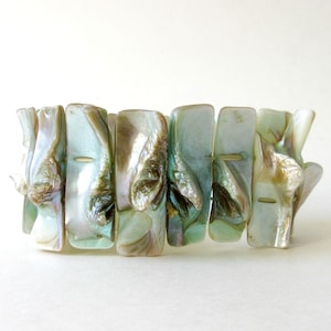 May include: A stretch bracelet featuring rectangular, iridescent, sea-green and brown shell segments. The bracelet has a natural, organic appearance, with each segment displaying unique patterns and textures. The bracelet is designed to fit a variety of wrist sizes.