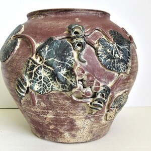 May include: A brown ceramic vase with a textured surface and a design of green leaves and grapes.