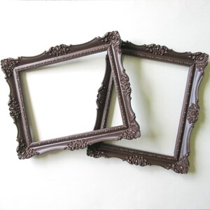 May include: Two dark brown picture frames with ornate, raised floral and scrollwork detailing along the edges. The frames are rectangular with a hollow center, featuring a matte finish and intricate relief patterns on all four sides of each frame.