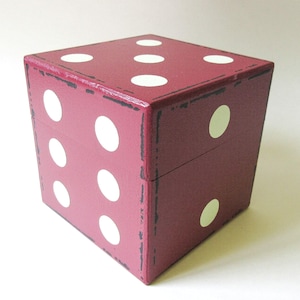 May include: A burgundy-colored, cube-shaped box designed to resemble a die. The box features white dots representing numbers, with a distressed finish and black trim. The box is a decorative item.