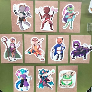 May include: A selection of fantasy character stickers on brown card. The stickers depict various anthropomorphic creatures, including an elephant, bear, frog, mouse, meerkat, pig, raccoon, axolotl, and cat. One sticker has the text "Roll for Panic Attack."