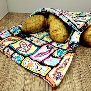 Può includere: Un sacchetto colorato e fantasia per conservare le patate contiene tre patate. Il sacchetto è aperto, rivelando le patate. Il design del sacchetto presenta un mix di forme floreali e geometriche in vari colori, tra cui rosa, giallo e blu.