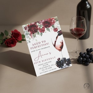 May include: A wine-themed birthday invitation with the text "Aged to Perfection!" and "Anna's 30th Birthday." The design features burgundy floral accents, a wine glass, and a pouring wine illustration. A bottle of wine, a glass of wine, and grapes are also present.