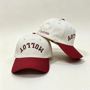 Peut inclure: Deux casquettes de baseball avec une calotte crème et une visière rouge foncé. La casquette avant affiche le mot MOLLOY en broderie rouge foncé. La casquette arrière présente le mot Custom et le texte partiel MOLLOY en broderie rouge foncé.