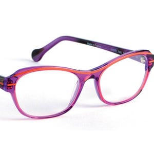 Op de afbeelding: Paarse en oranje bril met een cat-eye vorm. De monturen zijn fel paars met oranje accenten langs de randen en pootjes. De pootjes hebben een gestreept ontwerp in paars, oranje en zwart.