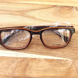 Peut inclure: Lunettes de vue rectangulaires avec une monture noire et marron. Les lunettes ont des verres transparents et sont partiellement recouvertes de plastique. La marque "J.F. Rey" est visible sur la monture.