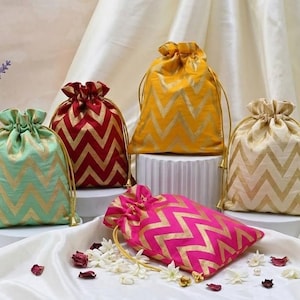 May include: A collection of drawstring pouches in various colors, including mint green, red, yellow, pink, and cream. Each pouch features a gold chevron pattern. The pouches are arranged on a white surface with floral accents.