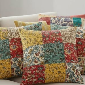 May include: A collection of decorative throw pillows with a patchwork design. The pillows feature a mix of floral patterns in red, yellow, and teal. The pillows are arranged on a white sofa, creating a cozy and inviting atmosphere.