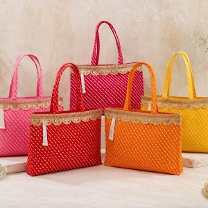 May include: Five rectangular tote bags in pink, red, magenta, orange, and yellow. Each bag features a diagonal white striped pattern, two top handles, and a decorative gold scalloped trim along the upper edge with a small white tassel.
