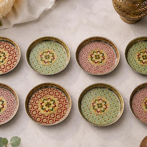 May include: A set of eight circular metal coasters featuring intricate floral patterns in shades of red, green, and pink. Each coaster has a metallic rim and a central mandala-style flower design with detailed geometric borders and gold accents.