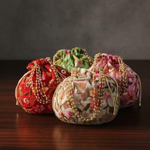 May include: Four round, embroidered drawstring pouches in red, green, white, and pink. Each pouch features intricate floral patterns and is adorned with beaded accents. The pouches are arranged on a dark wooden surface.