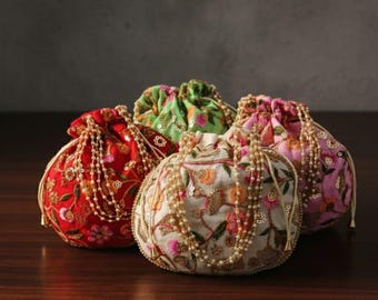 May include: Four round, embroidered drawstring pouches in red, green, white, and pink. Each pouch features intricate floral patterns and is adorned with beaded accents. The pouches are arranged on a dark wooden surface.