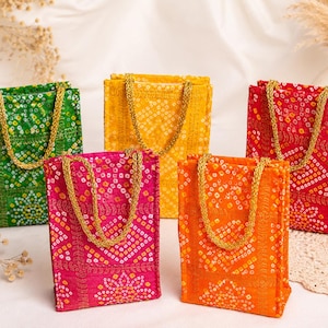 May include: Five rectangular fabric gift bags in green, yellow, red, pink, and orange. Each bag features a white tie-dye pattern, a grid-like texture, and two gold braided handles. The bags are arranged in a group, showcasing their vibrant colors.