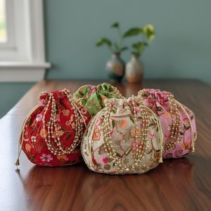 May include: Five embroidered drawstring pouches in red, green, pink, and beige. Each pouch features floral patterns, sequins, and beaded detailing. The pouches are displayed on a wooden surface, showcasing their intricate designs.