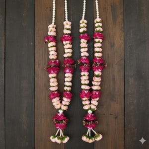 以下が含まれることがあります： 白いビーズの紐とピンクとバーガンディの花が交互に並んだ4つの花のガーランド。ガーランドは、暗い木製の背景に吊り下げられています。ガーランドは、装飾や特別な機会に使用される可能性があります。