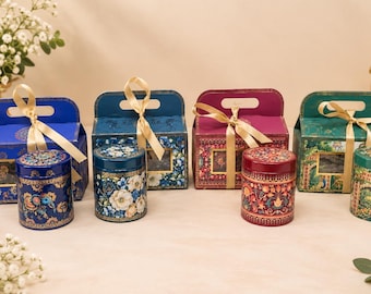 Può includere: Quattro scatole regalo rettangolari con manici e barattoli cilindrici abbinati, ognuno con intricati motivi floreali e decorativi in blu, blu scuro, magenta e verde. Ogni scatola è legata con un nastro dorato e presenta una finestra trasparente.