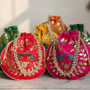 May include: A collection of colorful, round drawstring bags. The bags are in shades of red, pink, green, yellow, and orange. Each bag is adorned with gold embroidery, pearl accents, and a peacock design. The bags are arranged on a light-colored surface.