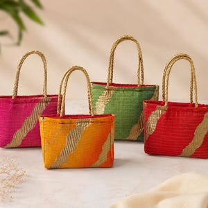Peut inclure: Quatre petits sacs à main rectangulaires en tissu avec des anses dorées tressées. Chaque sac présente une surface texturée dans des tons unis rose, orange, vert et rouge, rehaussée d'une bande dorée métallique ondulée en diagonale.