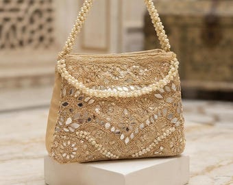 May include: A gold-toned handbag featuring intricate embroidery, small inset mirrors, and a handle crafted from rows of white pearls. The bag is adorned with detailed floral patterns and metallic thread work, complemented by a matching pearl-embellished accessory.