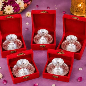 May include: Five silver-colored metal oil lamps, each featuring a circular base with intricate embossed patterns and a shallow bowl top, are individually presented inside open, bright red velvet-lined boxes with gold-toned metal latches.