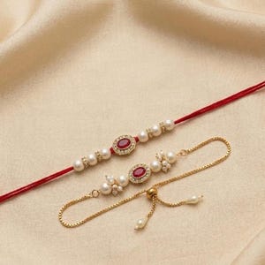 May include: A red thread bracelet featuring a central oval red stone surrounded by small white pearls and crystals, alongside a gold-tone chain bracelet with a matching oval red stone, white pearl clusters, and a sliding adjustable clasp.