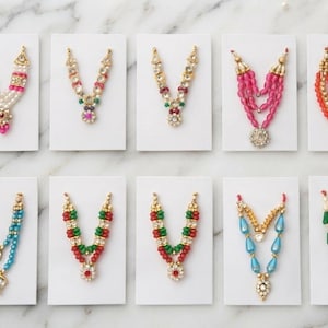 May include: Ten decorative necklaces displayed on individual white cards. The necklaces feature various arrangements of colorful beads, faux pearls, and metallic accents in shades of pink, red, green, blue, orange, and gold, with intricate central pendants.