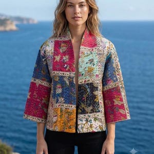 Puede incluir: Una chaqueta acolchada con un diseño de patchwork que presenta varios patrones florales y botánicos en tonos rosa, azul, amarillo y blanco. La chaqueta tiene una parte frontal abierta, mangas tres cuartos y costuras visibles en la tela.