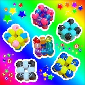May include: A collection of colorful beaded creations, including pink, blue, yellow, and clear beads. The beads are arranged in various shapes and patterns, set against a vibrant rainbow gradient background with star accents.