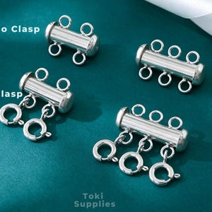 May include: Four silver-toned jewelry multi-strand connectors. Two are labeled No Clasp with two or three loops, and two are labeled With Clasp, featuring attached spring ring clasps. The text Toki Supplies is visible at the bottom of the image.
