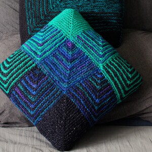 Puede incluir: Dos almohadas de crochet con patrones geométricos en tonos de verde, azul y negro.