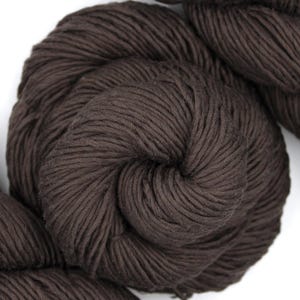 May include: Close-up of dark brown yarn skeins. The yarn is tightly wound, showing the texture of the fibers. The color is a rich, solid brown, suitable for various knitting or crochet projects. The image is set against a white background.