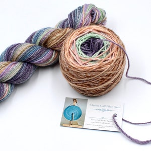 Peut inclure: Une pelote de fil teinte à la main dans des tons de brun, violet, vert et bleu. Le fil est enroulé en boule et prêt à être utilisé pour le tricot ou le crochet. Le fil est étiqueté "Clarion Call Fiber Arts".