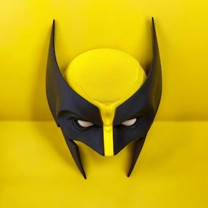 Può includere: Una maschera da supereroe gialla e nera con aperture bianche per gli occhi. La maschera ha una parte superiore gialla strutturata e lati neri con punte appuntite. Lo sfondo è giallo pieno.
