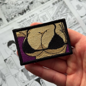 May include: Embroidered patch depicting a stylized bust in a black bikini top. The patch has a black border, a purple background, and gold and black detailing. The patch is rectangular in shape.