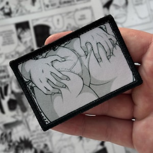 Puede incluir: Un parche rectangular con borde negro presenta una ilustración en escala de grises de estilo anime de manos tocando las nalgas de una persona. El fondo está borroso con paneles de manga.