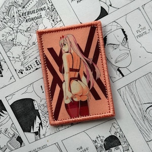 May include: A rectangular patch with a peach background featuring an anime-style illustration of a woman in lingerie. The patch has a maroon border and a maroon "X" design. The background includes manga panels.