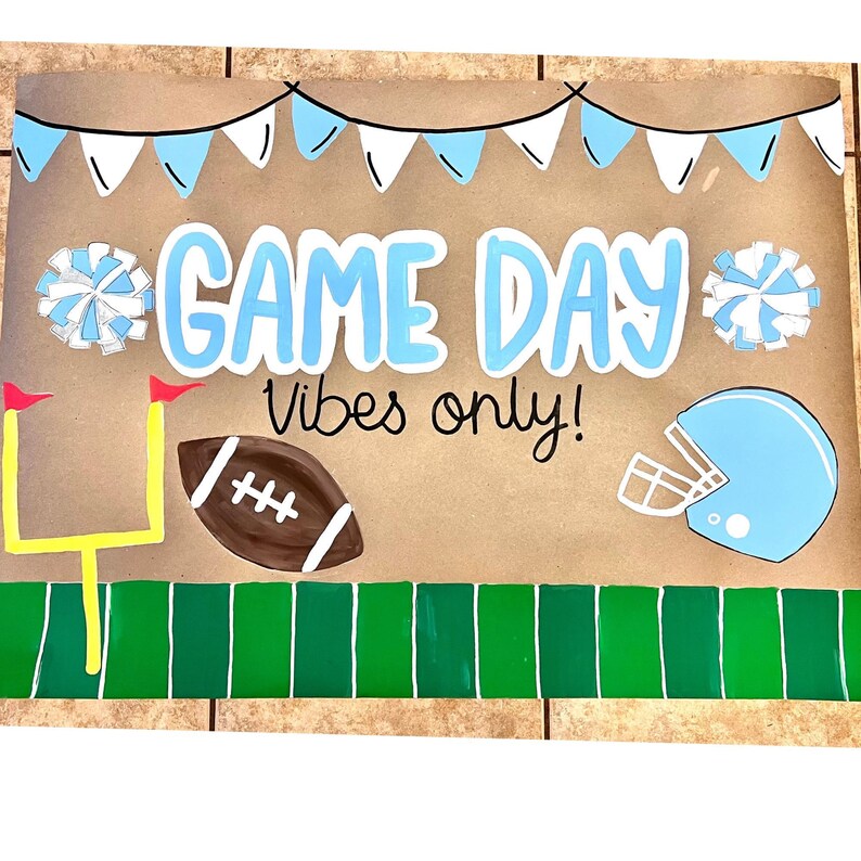 The image is a vibrant and colorful sign that reads "GAME DAY VIBES ONLY!" The sign is adorned with various football-related elements, such as a football, a cheerleader, and a football helmet, all set against a green background.