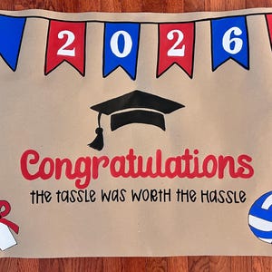 The image is a graduation-themed banner with the year "2026" displayed, a graduation cap, and a volleyball. The text "Congratulations the tassel was worth the Hassle" is written below the graduation cap.