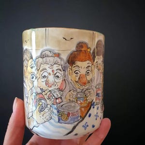 May include: Hand-painted ceramic mug featuring a whimsical illustration of several elderly people. The artwork depicts the figures with exaggerated features, holding cans and other items. The mug has a light beige background with a blue and white patterned base.