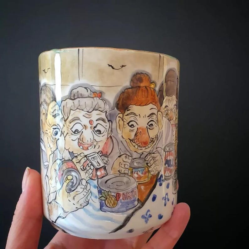 May include: Hand-painted ceramic mug featuring a whimsical illustration of several elderly people. The artwork depicts the figures with exaggerated features, holding cans and other items. The mug has a light beige background with a blue and white patterned base.