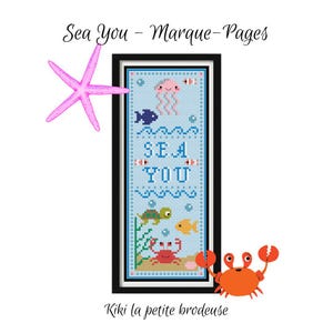 Peut inclure: Une broderie au point de croix encadrée avec les mots "SEA YOU" en bleu, représentant des créatures marines telles qu'une méduse, un poisson, une tortue et un crabe. Une étoile de mer rose et un crabe orange sont également présents. Le texte "Sea You - Marque-Pages" est en haut.