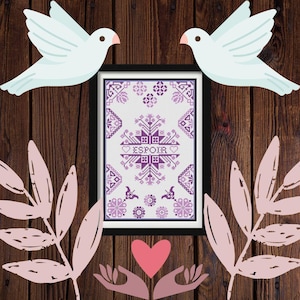 May include: A framed cross-stitch artwork with a purple and white floral design and the word "ESPOIR". Two white doves and pink leaves are arranged around the frame on a wooden background. A pink heart and hands are at the bottom.