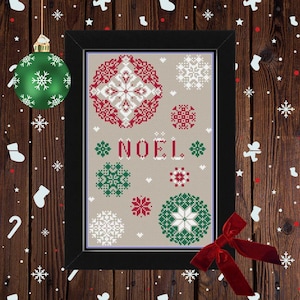 Peut inclure: Une œuvre d'art au point de croix encadrée avec un fond beige, présentant des motifs de flocons de neige rouges, blancs et verts. Le mot "NOEL" est brodé en rouge et blanc. L'œuvre est dans un cadre noir, avec un nœud rouge et des ornements de Noël en arrière-plan.