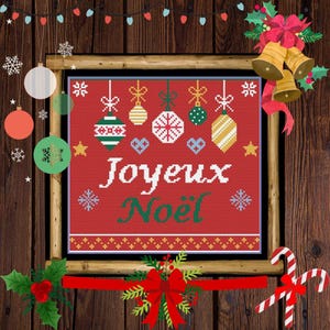 May include: A framed cross-stitch design with the words "Joyeux Noël" in white and green on a red background. The design features hanging ornaments and snowflakes, with a wooden background and Christmas decorations.