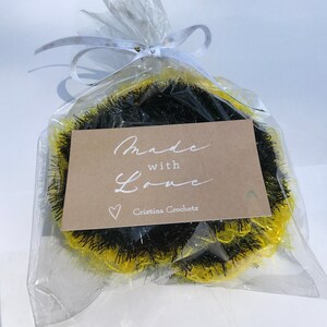 May include: A black and yellow crocheted wreath with a brown tag that says "Made with Love" and "Cristina Crochets".